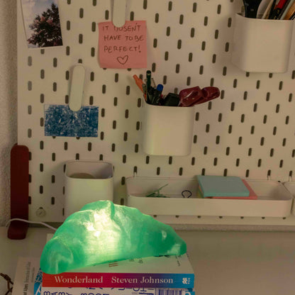 Desk setup with pegboard, books, and a glowing green croissant lamp.