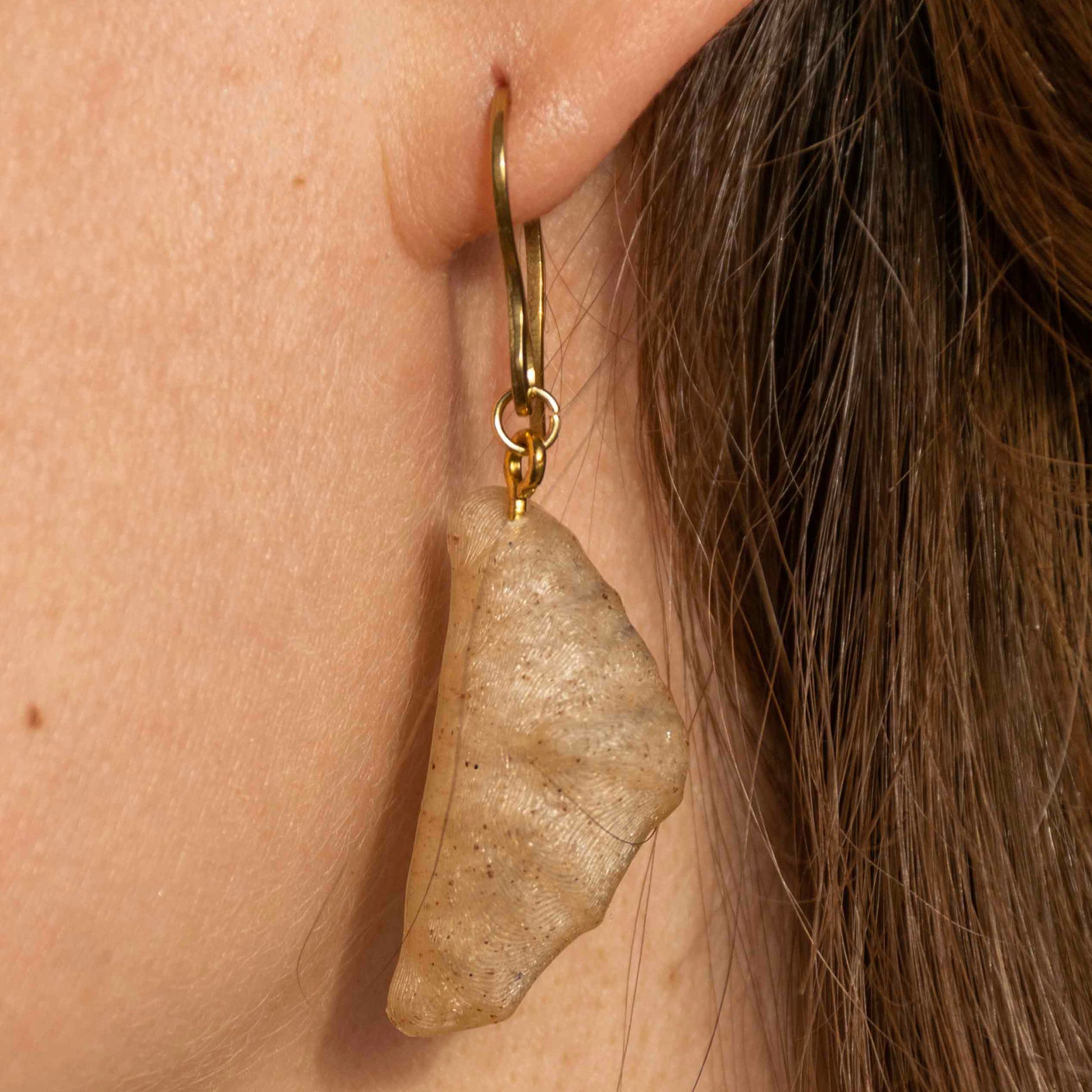 Close-up of a person wearing a wheat croissant earring with gold hoop.