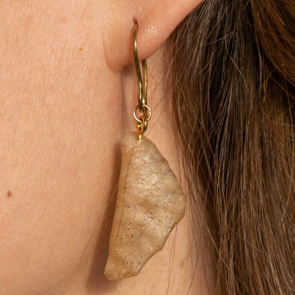 Close-up of a person wearing a wheat croissant earring with gold hoop.