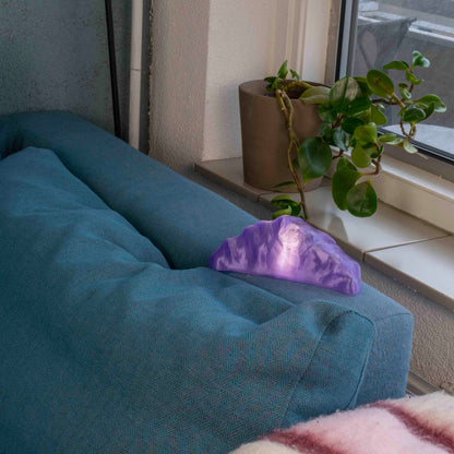 Purple croissant lamp on a blue couch with a plant in the background