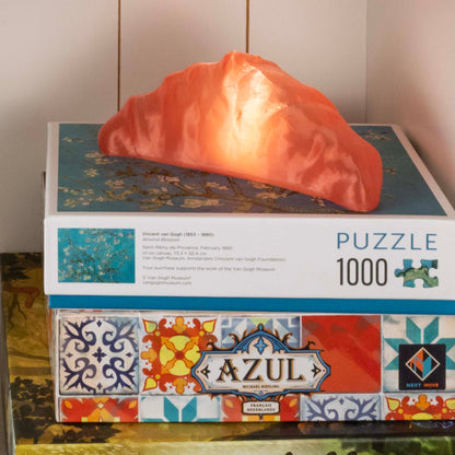 Pink croissant lamp on a puzzle box with a colorful design on a neutral background