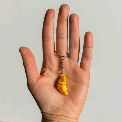 Hand holding a keychain shaped like a golden croissant against a plain background